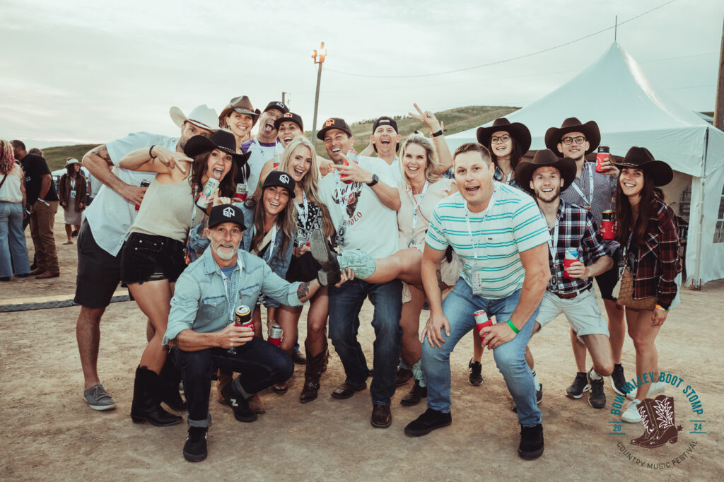 A group of people pose for a picture. They are partying and having a good time, lots of them are wearing cowboy hats.