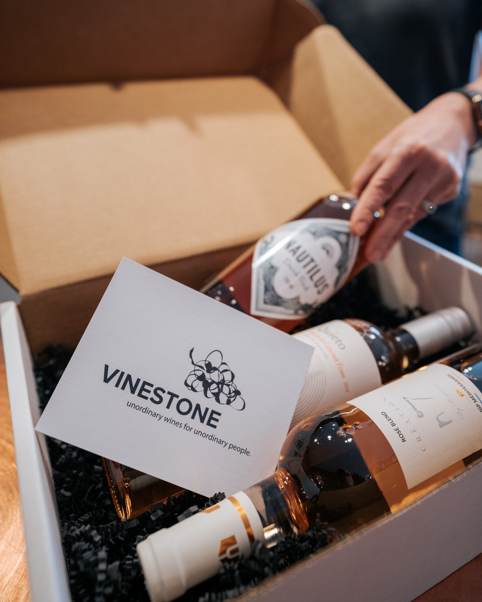 A hand places the last of three bottles of rose wine into a box.